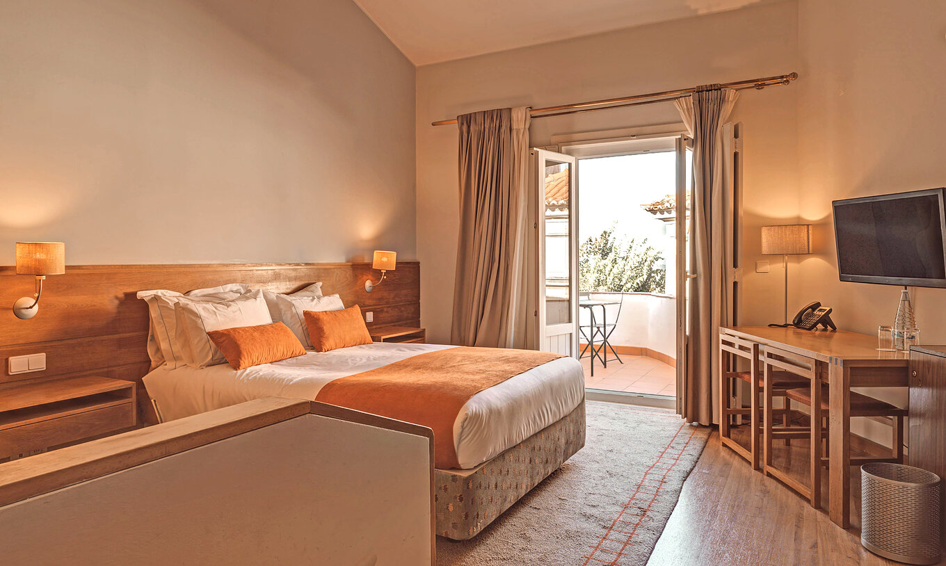 La Habitación Superior Varanda de la Pousada Ourém tiene una cama matrimonial y acceso a una terraza con mesa y silla