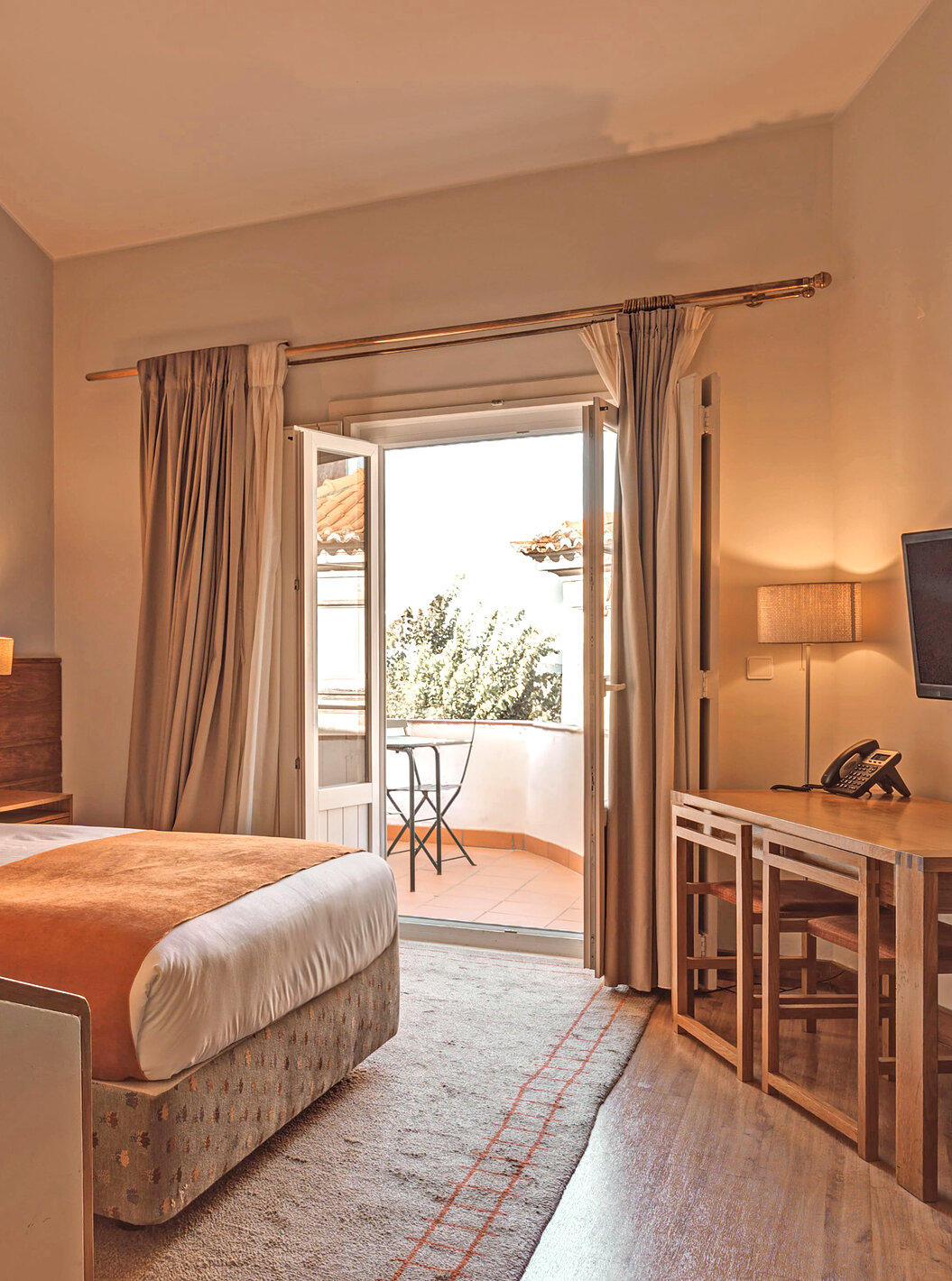 La Habitación Superior Varanda de la Pousada Ourém tiene una cama matrimonial y acceso a una terraza con mesa y silla