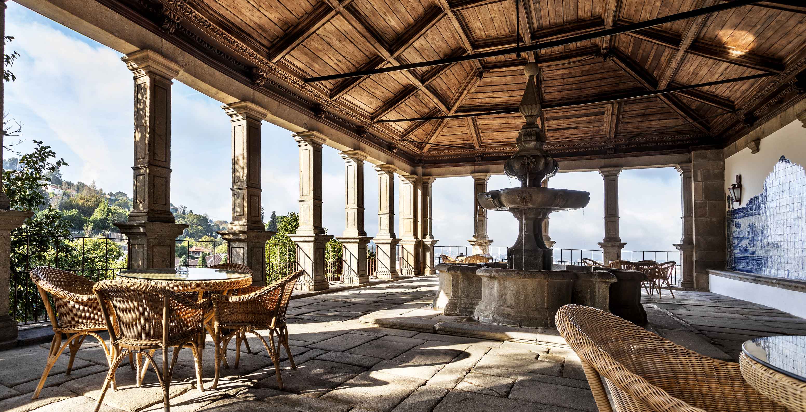 Terraza cubierta de la Pousada Mosteiro de Guimarães, con vistas a la ciudad y una fuente de piedra en el centro