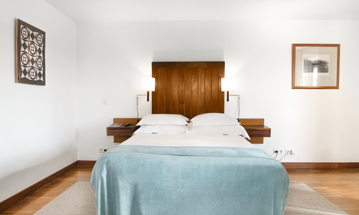 La Junior Suite de la Pousada Castelo Alcácer do Sal a un lit double avec une couette bleue, et tête de lit en bois