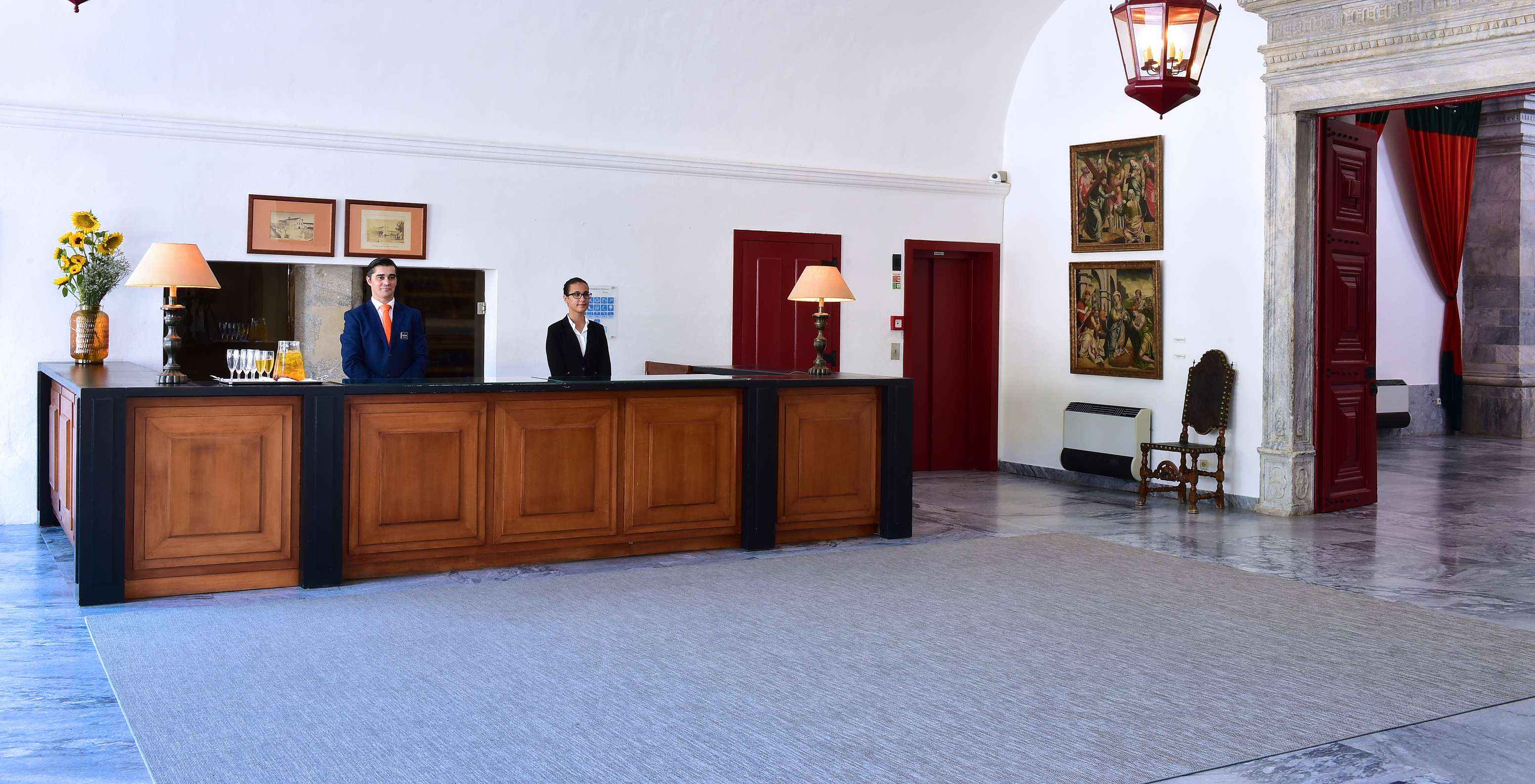 Réception de l'hôtel avec piscine à Beja, avec deux membres de l'équipe Pestana prêts à accueillir les prochains invités