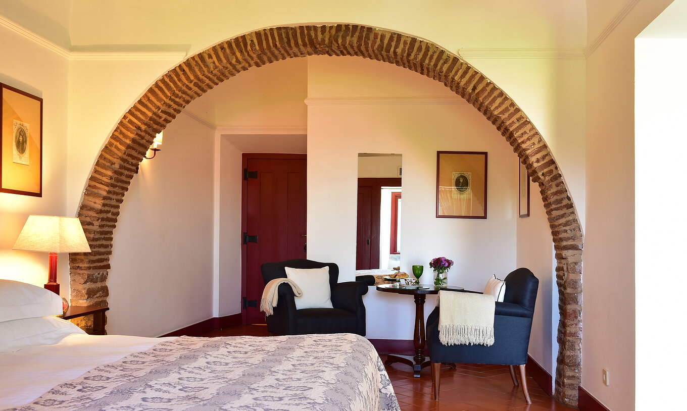 La Junior Suite de la Pousada Convento Beja a un arc à l'intérieur de la chambre au-dessus de deux fauteuils bleus