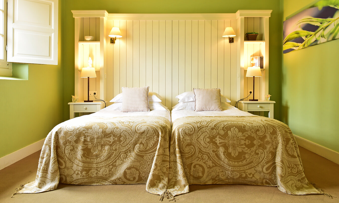 Le Chambre Classique de la Pousada Convento Évora compte deux lits séparés avec une couverture beige à motifs et murs verts