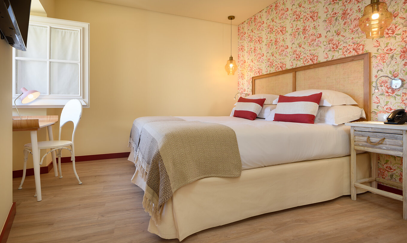 Le Chambre Supérieure de la Casa Lidador - Óbidos a un lit double papier peint fleuri et un bureau devant la fenêtre