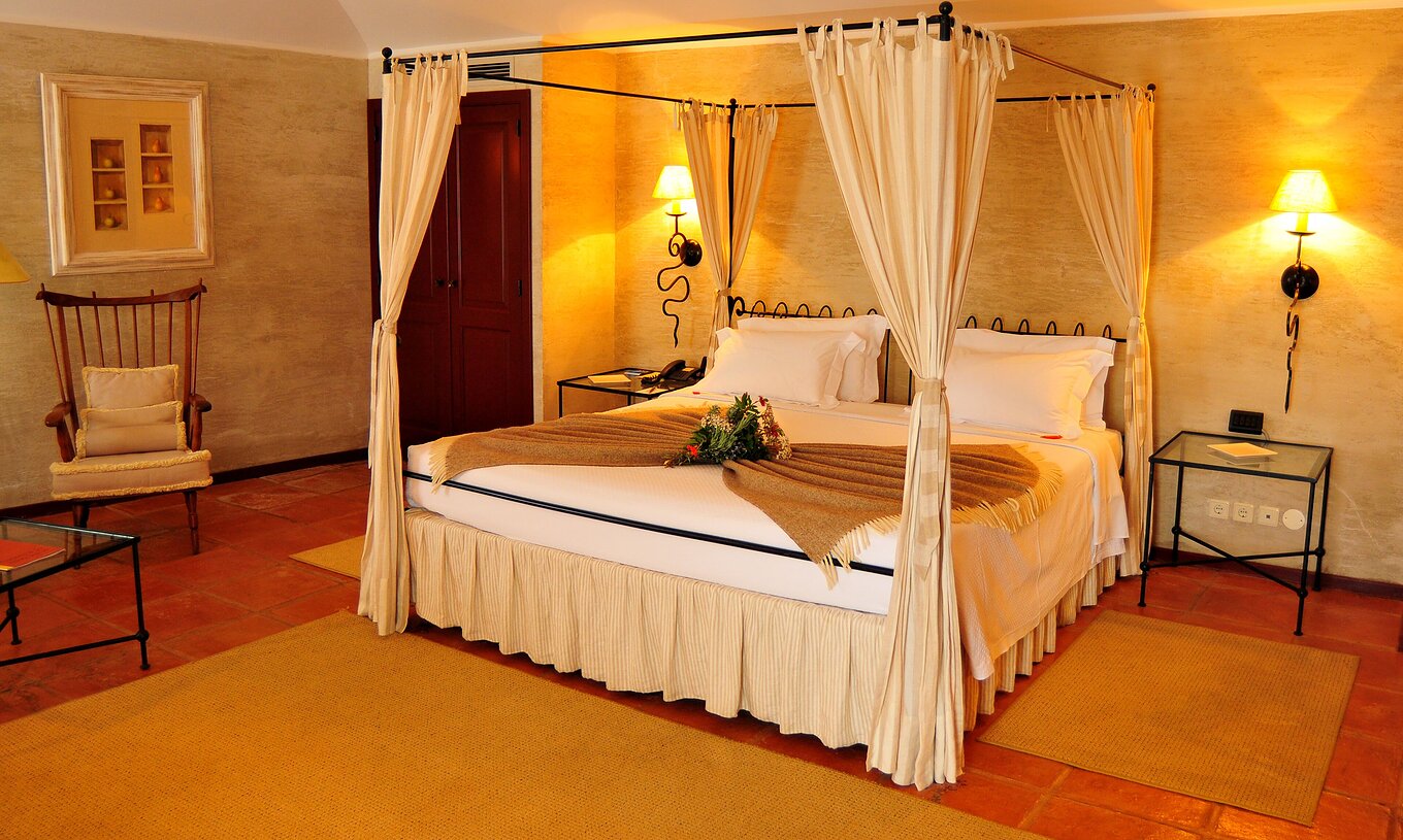 Le Chambre Supérieur de la Pousada Convento de Belmonte a un lit double avec une couverture et des fleurs sur le lit