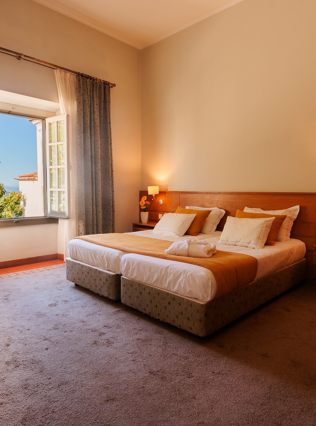 La Suite de la Pousada Ourém a un lit double avec une couette orange et une fenêtre ouverte à côté