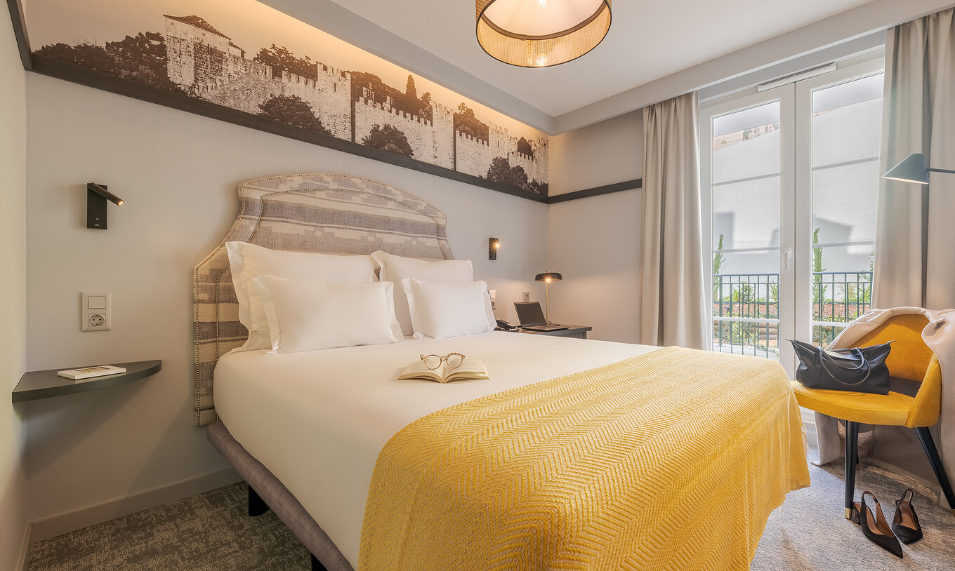 Le Comfort Balcony de la Pousada Alfama dispose d’un lit double avec des draps blancs, un plaid jaune et un petit balcon