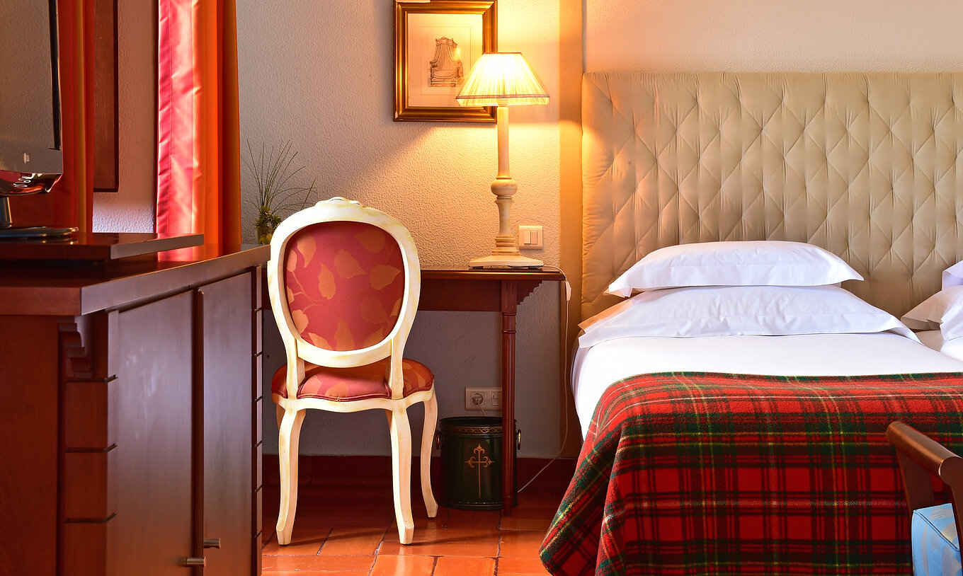 Le Superior Familial de la Pousada Castelo Palmela a un lit avec draps blancs et une couverture à carreaux, et bureau en bois