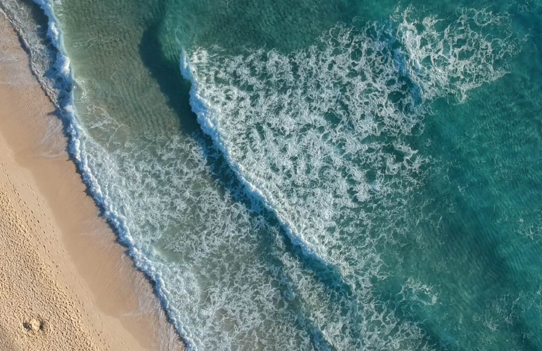 Vue aérienne d'une plage avec des vagues se brisant sur le sable doré, dans un hôtel du groupe Pestana