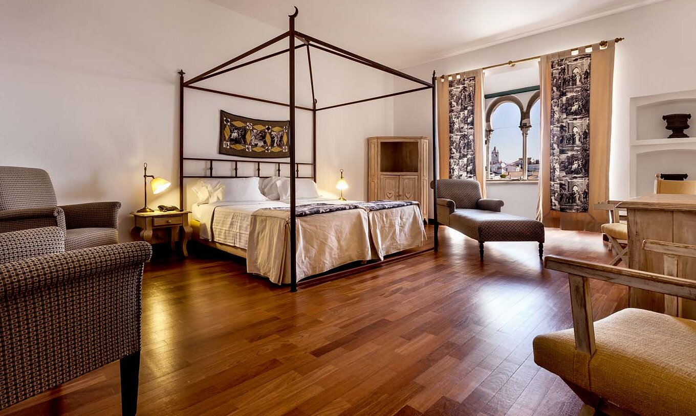 De Standaard Suite van Pousada Castelo Alvito heeft twee bedden, een fauteuil en een raam met bogen en uitzicht op het dorp