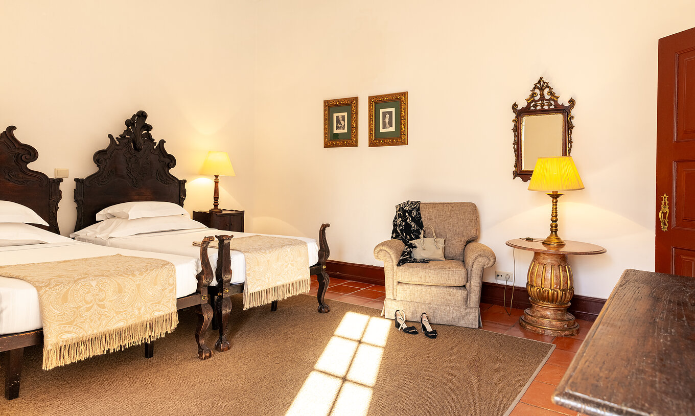 De Superior Familiale Kamer van Pousada Castelo Estremoz heeft twee eenpersoonsbedden van donker hout met een gele dekbed