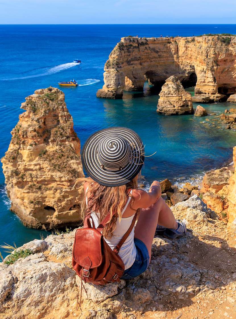 Vrouw bewondert het panoramische uitzicht op de Algarve-kust, met kristalhelder water en een door vegetatie omgeven klif