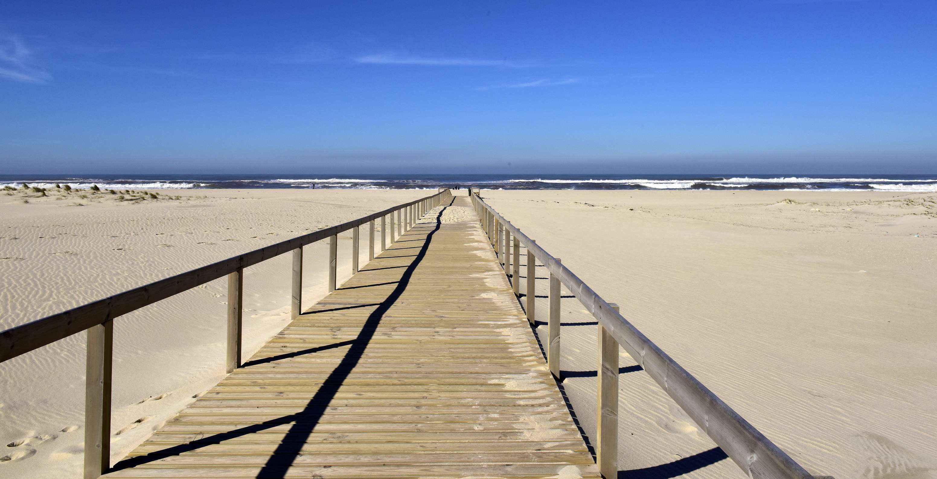 Strand van Aveiro met een houten promenade witte zand en de zee met enkele golven op de achtergrond