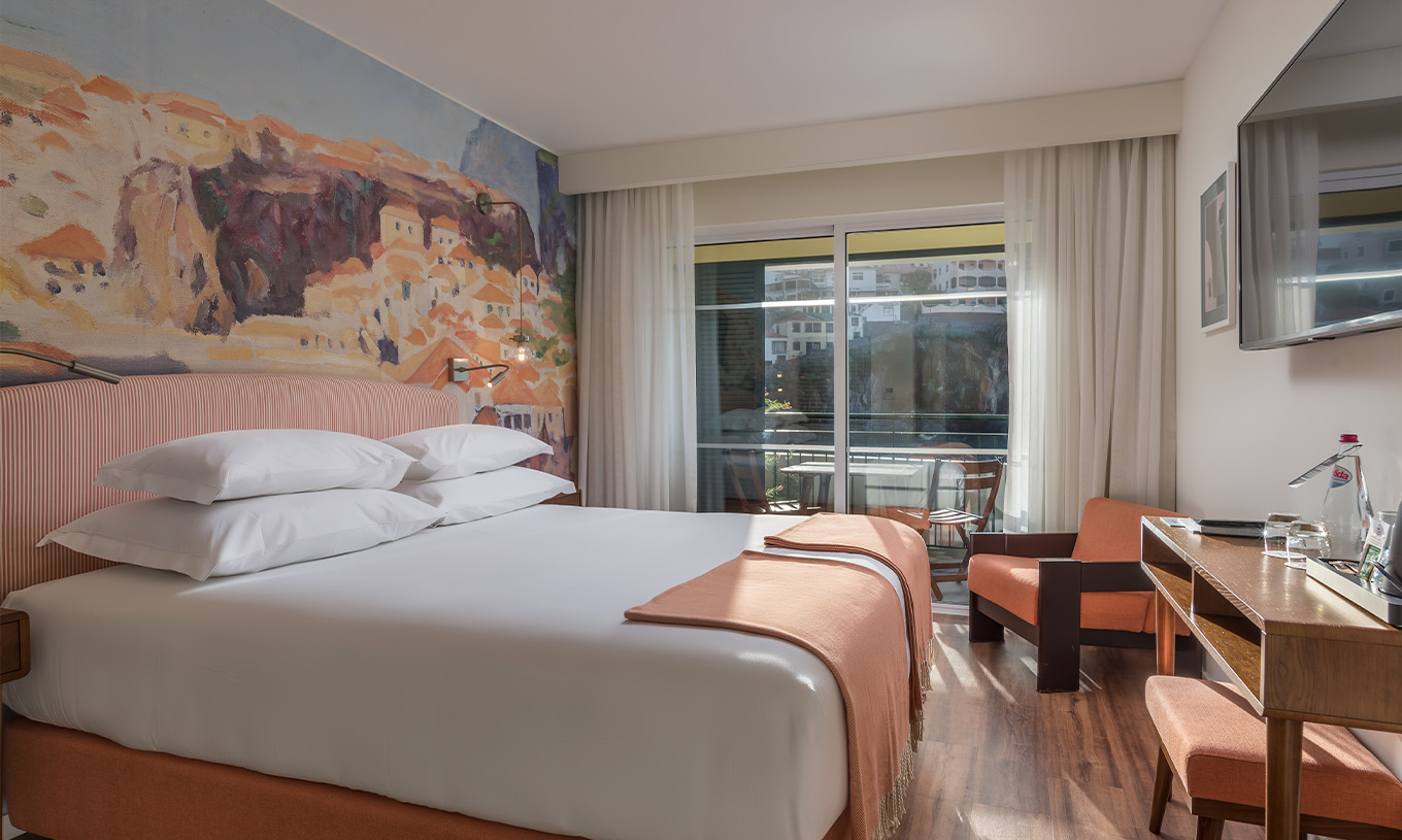 De Deluxe Bay View Room van Pestana Churchill Bay heeft zalmroze tinten, een tweepersoonsbed, balkon en fauteuil