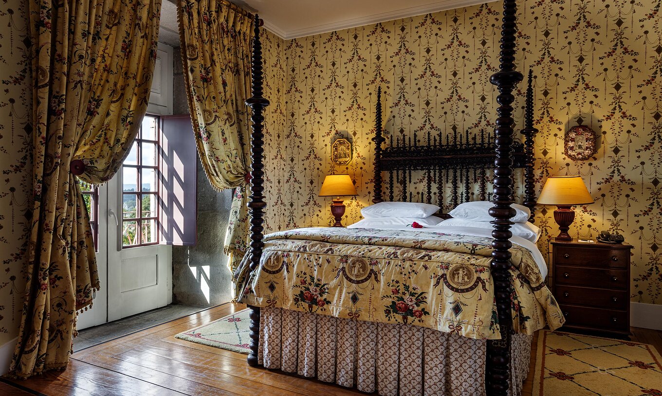 Het Master Suite van Pousada Mosteiro Guimarães heeft een tweepersoonsbed van donker hout en behang met patroon
