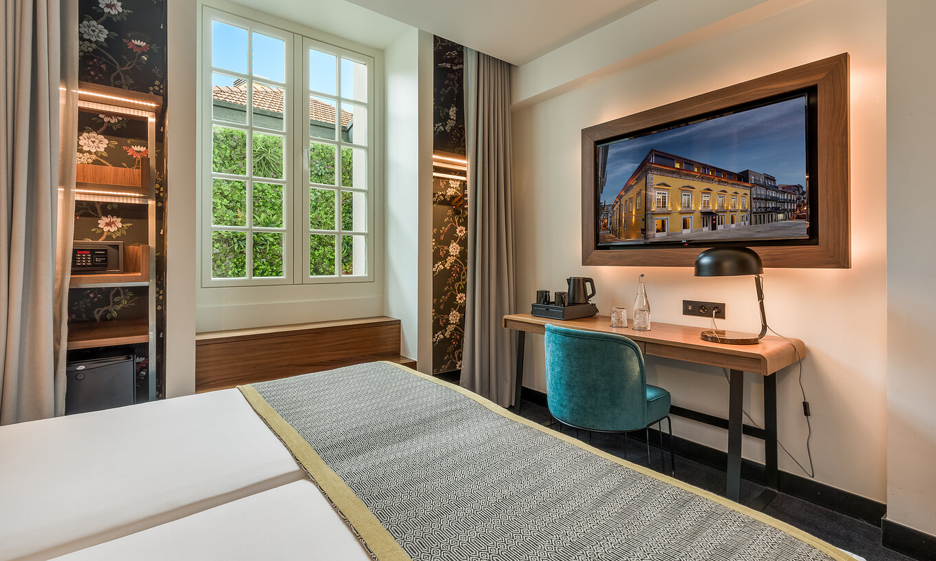 De Cozy Room van Pousada Porto - Rua das Flores heeft een bureau aan het voeteneinde van het bed en een televisie erbovenop.