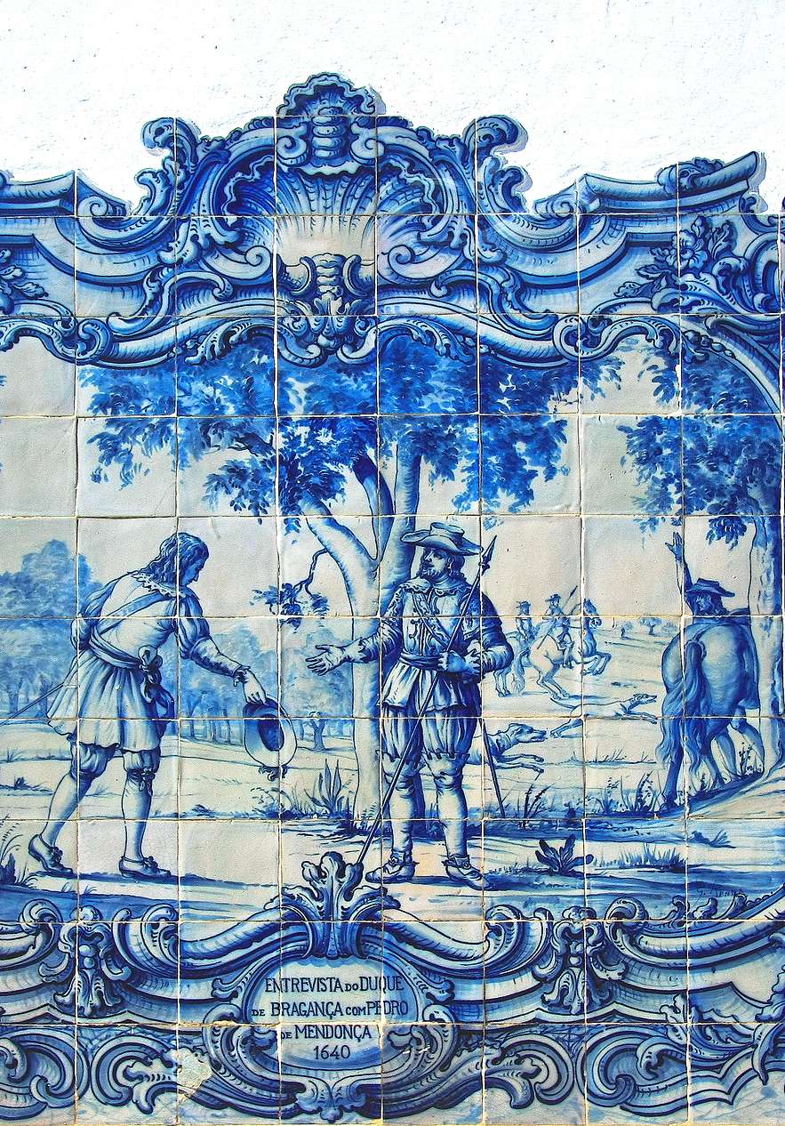 Painel de azulejos azuis e brancos com moldura ornamental retratando cena histórica com figuras em paisagem
