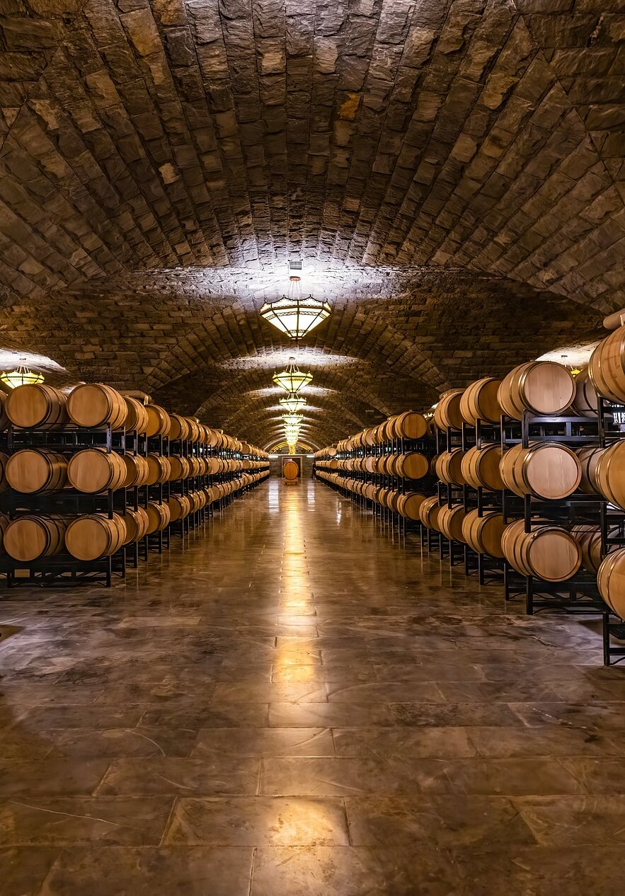 Adega com fileiras de barris de vinho perto da Pousada Convento Beja, Hotel Histórico em Beja, sob arcos de pedra