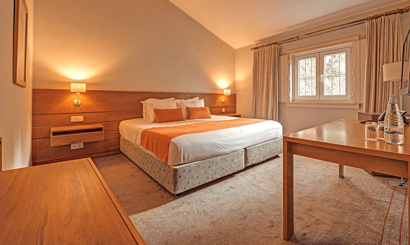O Quarto Clássico da Pousada Ourém tem uma cama de casal com uma janela e cortinas cinzentas