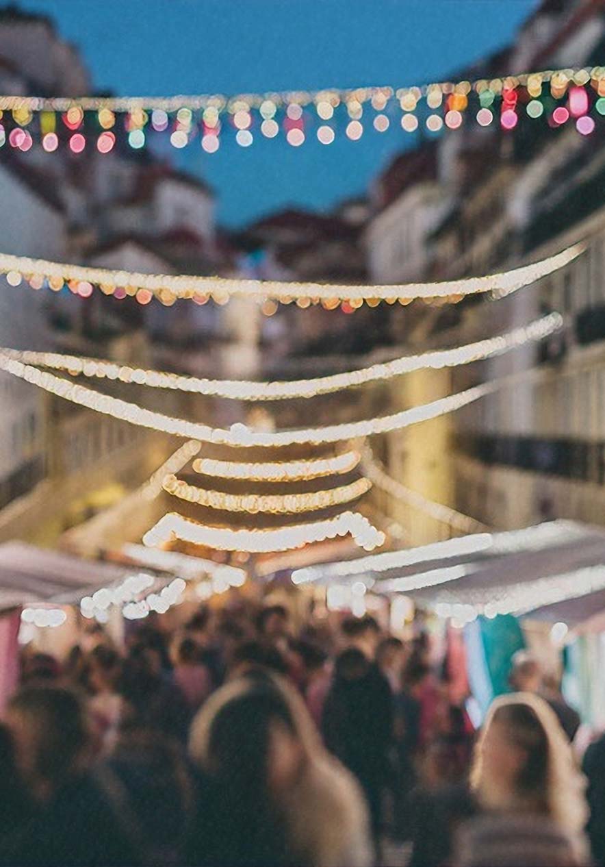 Festa de Santo Antônio em Lisboa com ruas iluminadas, barracas e visitantes caminhando à noite movimentada