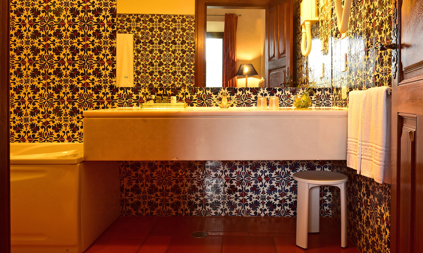 A Master Suite da Pousada Castelo Palmela tem uma casa de banho com lavatório com espelho, toalhas e um pequeno banco