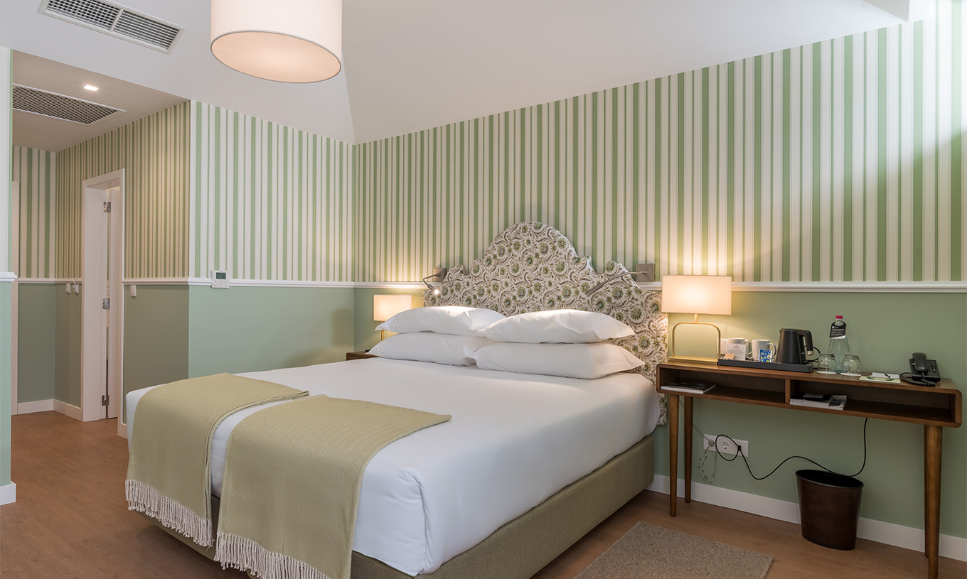 O Quarto Clássico do Pestana Churchill Bay tem uma cama de casal, papel de parede às riscas em tons verdes e uma mesa