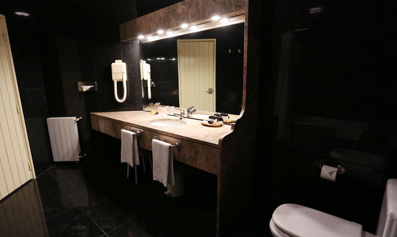 O Quarto Clássico da Pousada Valença tem uma casa de banho escura com lavatório, toalhas e sanita