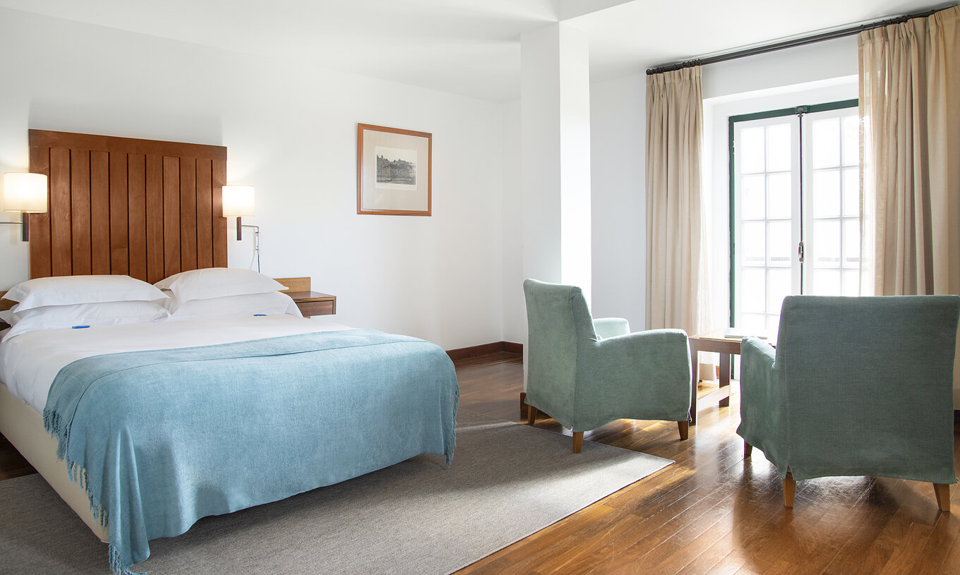 A Junior Suite da Pousada Castelo Alcácer do Sal tem uma cama de casal com uma colcha azul, dois cadeirões e janela