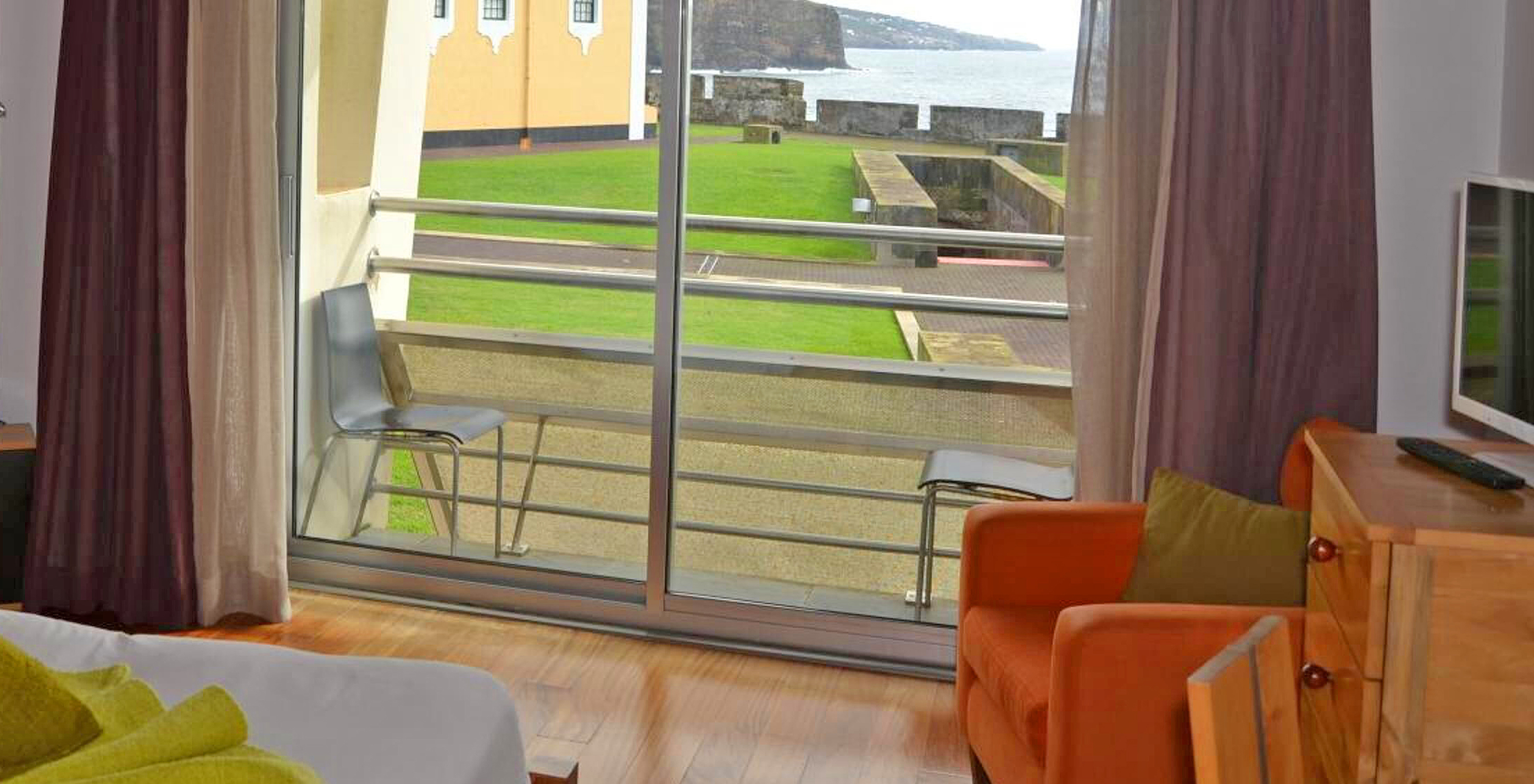 O Quarto Clássico da Pousada Forte Angra do Heroísmo tem uma pequena varanda com duas cadeiras e vista para o mar