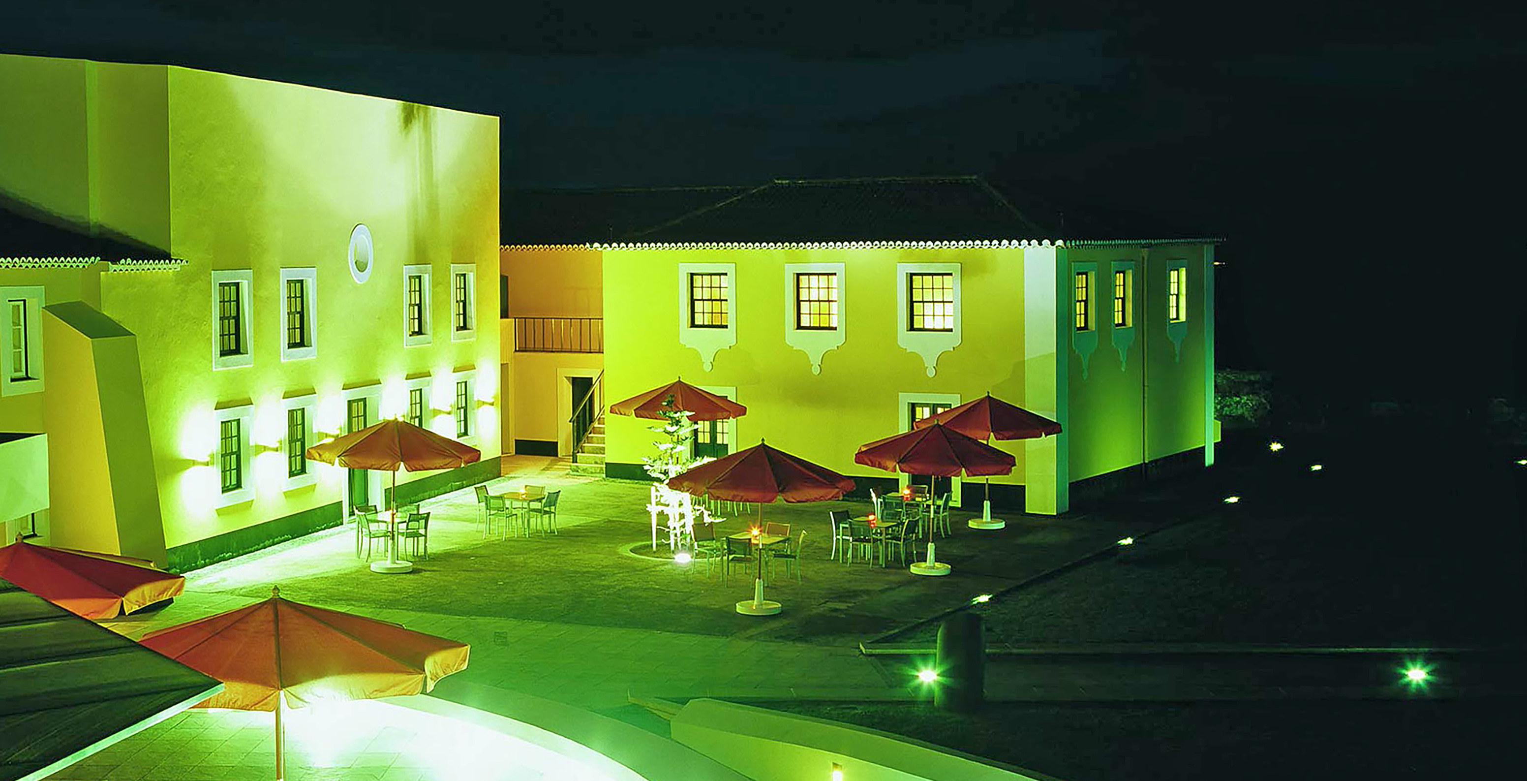 Edifícios da Pousada Forte Angra do Heroísmo com um pátio com uma esplanada com mesas, cadeiras e chapéus-de-sol
