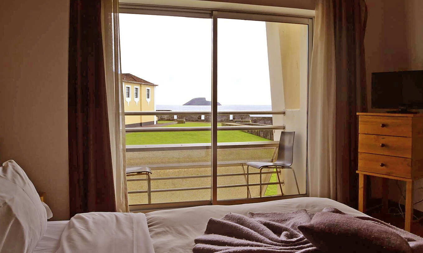 O Quarto Superior da Pousada Forte Angra do Heroísmo tem uma cama, televisão e varanda com duas cadeiras e vista para o mar