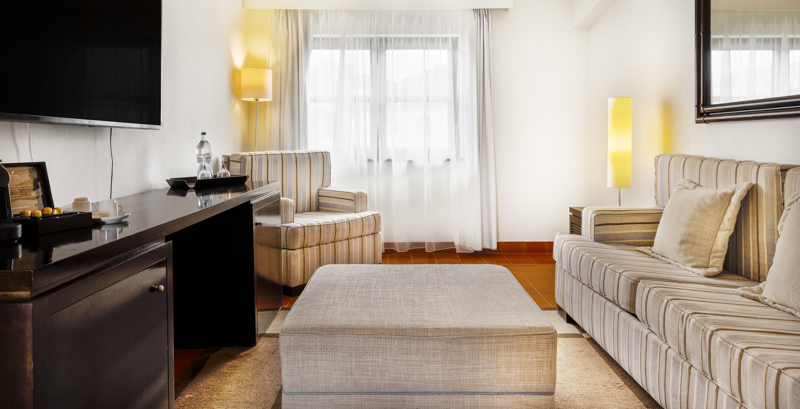 O quarto Master Suite da Pousada Forte Horta tem uma cama de casal, um cadeirão, uma televisão e uma janela grande