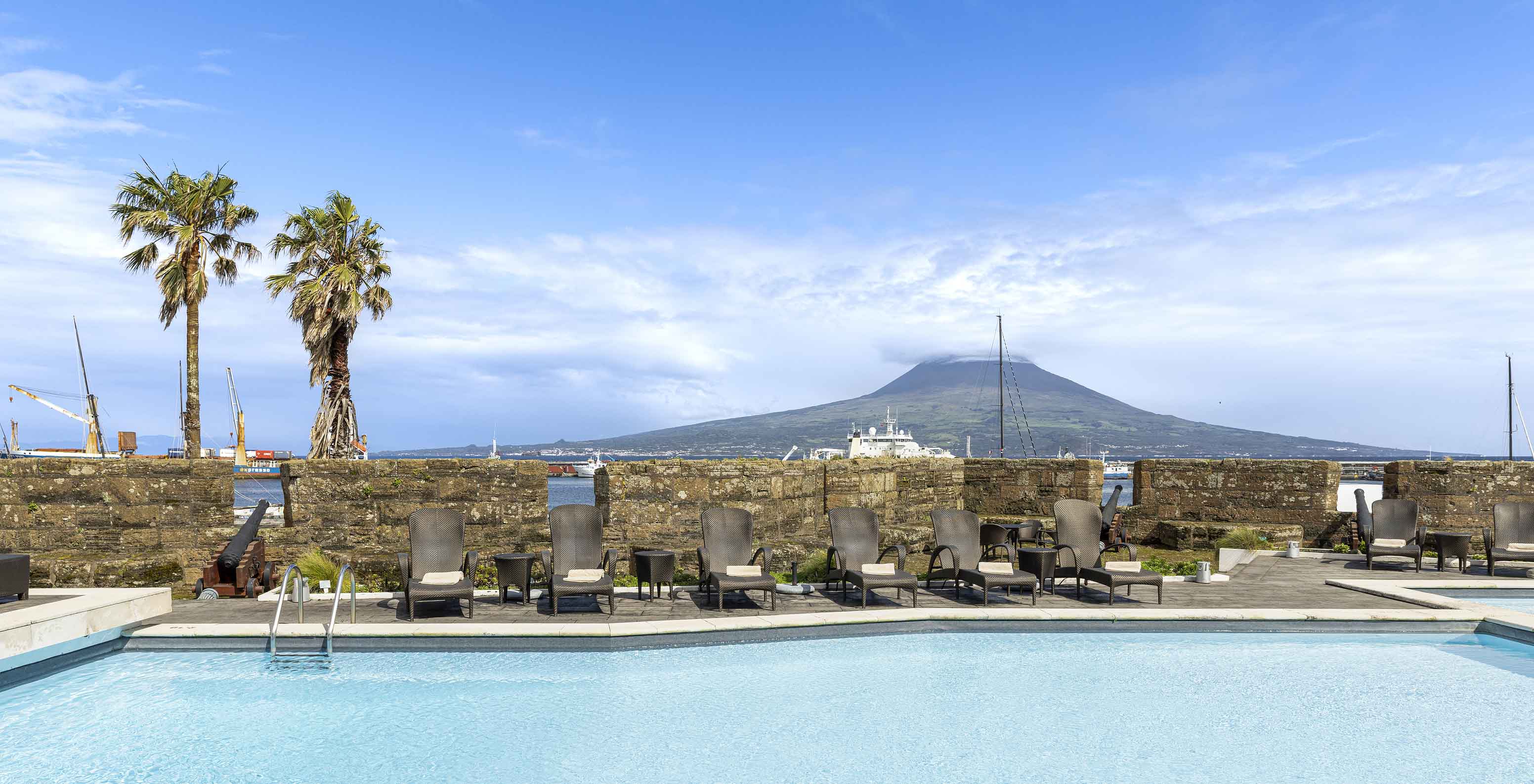 Piscina exterior da Pousada Forte Horta, um hotel histórico nos Açores, com vista para o Pico e várias espreguiçadeiras