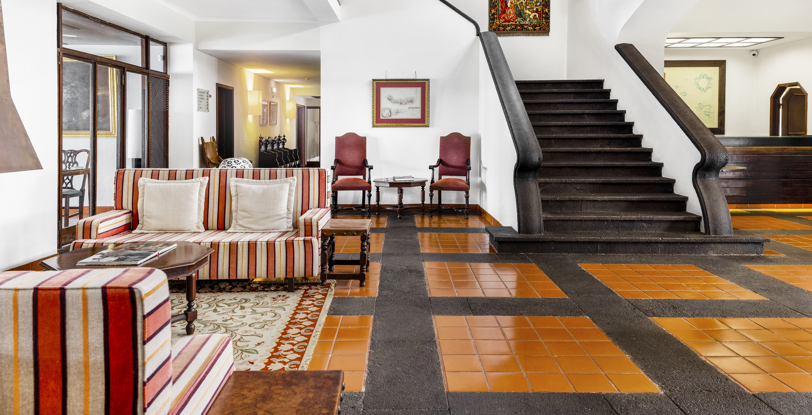 A Pousada Forte da Horta, hotel histórico nos Açores, tem um hall com sofás com riscas, cadeiras e umas escadas