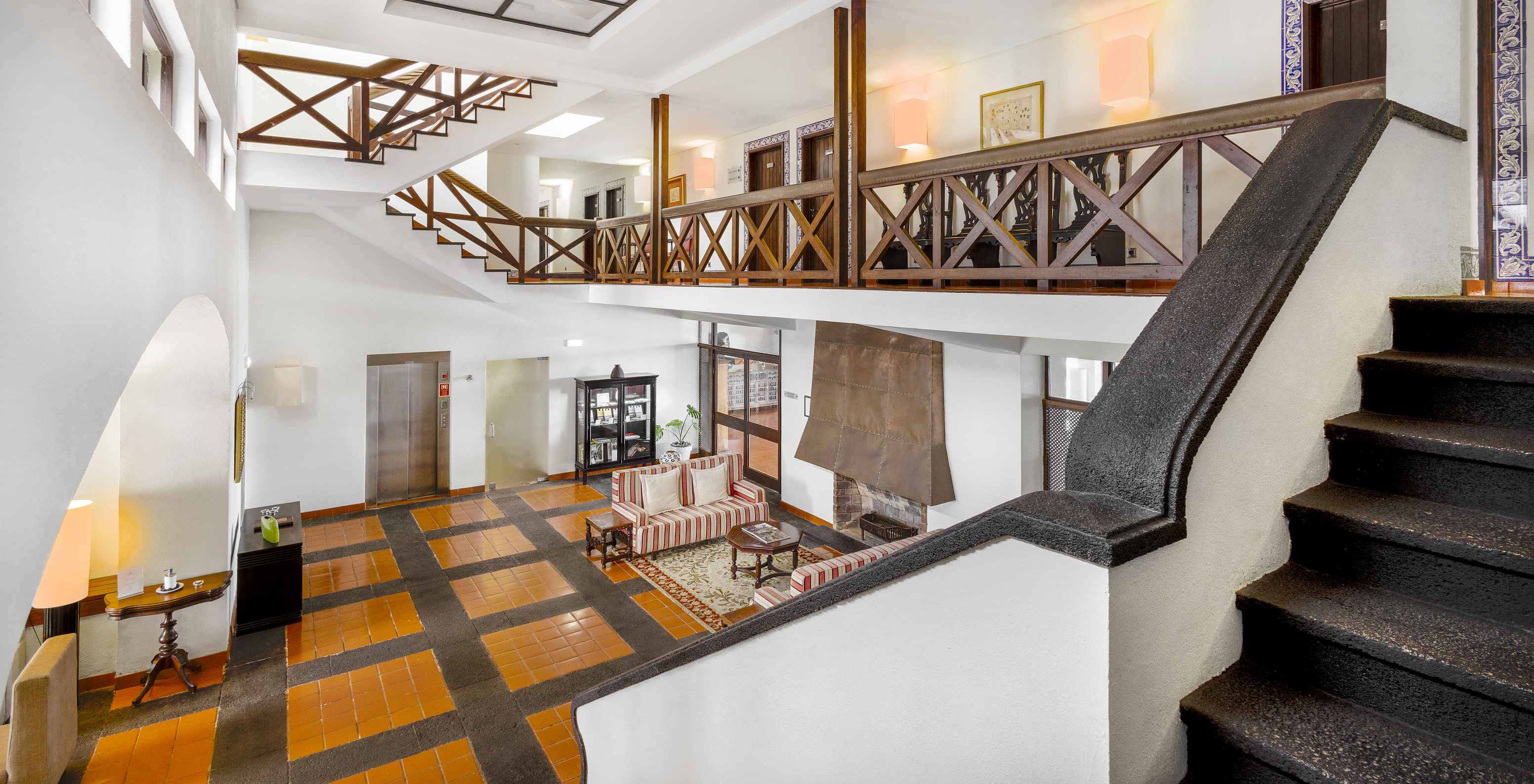 Fachada interior da Pousada Forte da Horta, com dois pisos, paredes brancas com madeira, e sofás