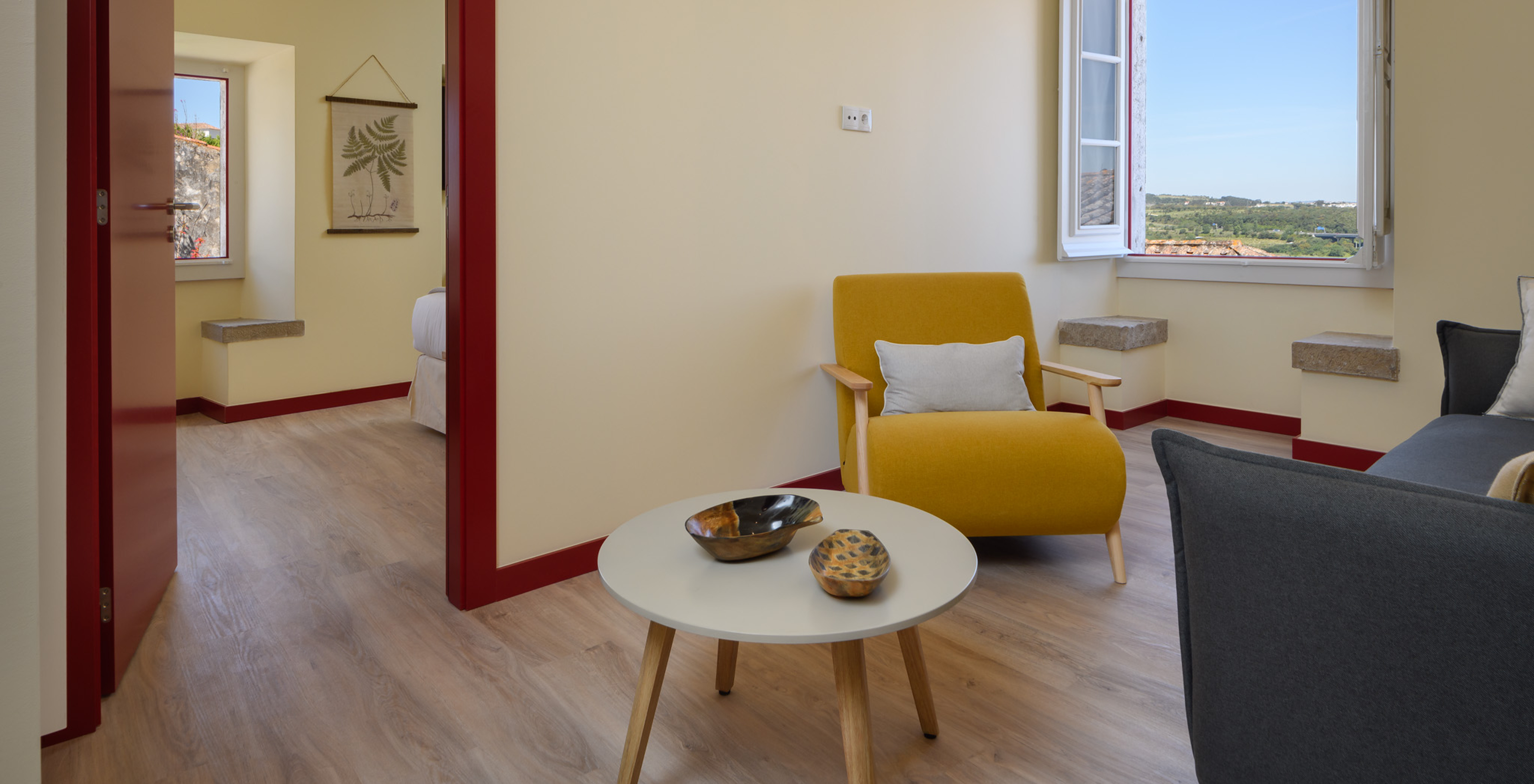 A Suite da Casa Lidador - Óbidos tem uma pequena sala com sofá , cadeira, mesa e apoio e uma janela com um banco em pedra