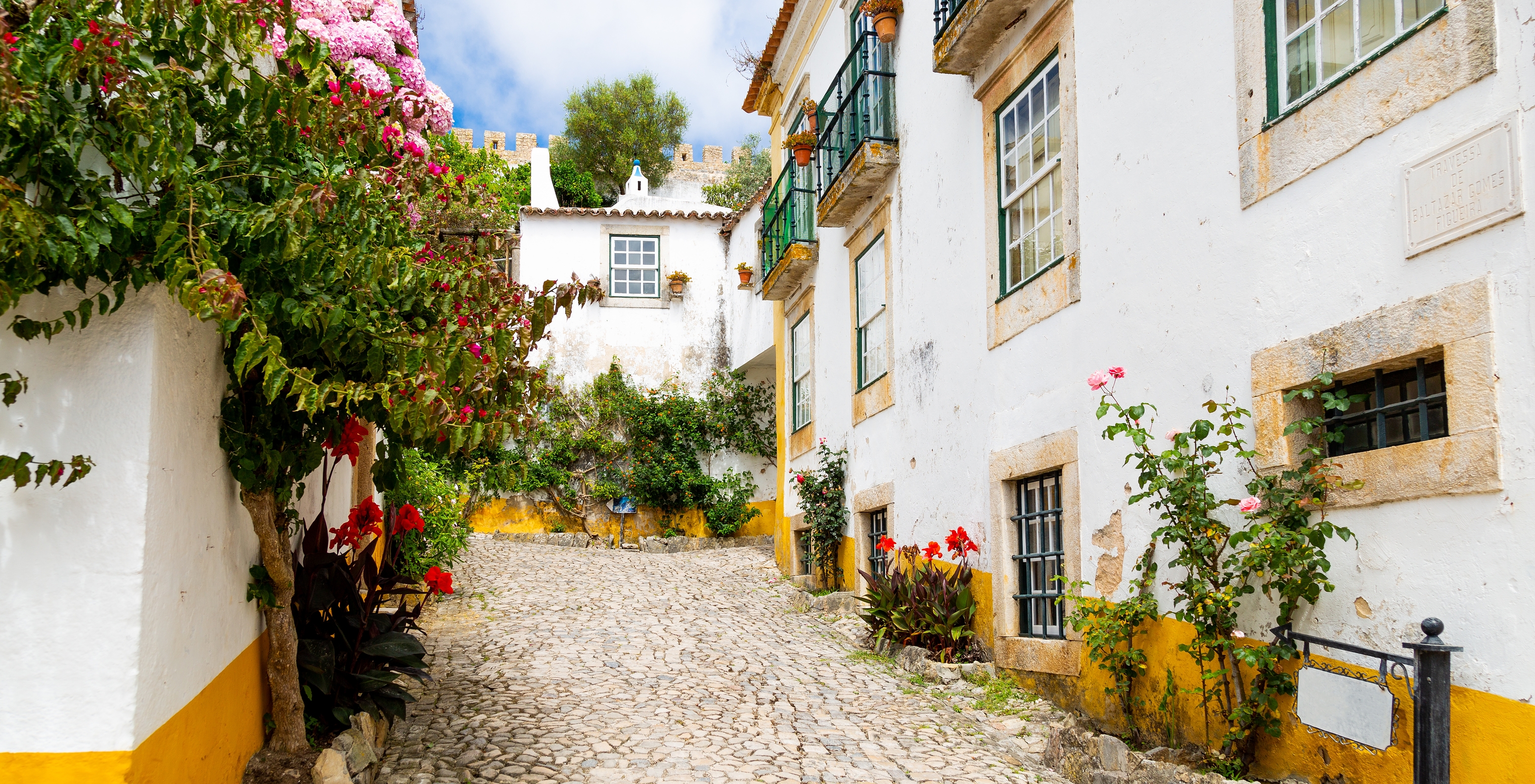 Vila de Óbidos, com várias casas com telhados em ardósia, caiadas de branco, ruas estreitas e o Castelo de Óbidos ao fundo