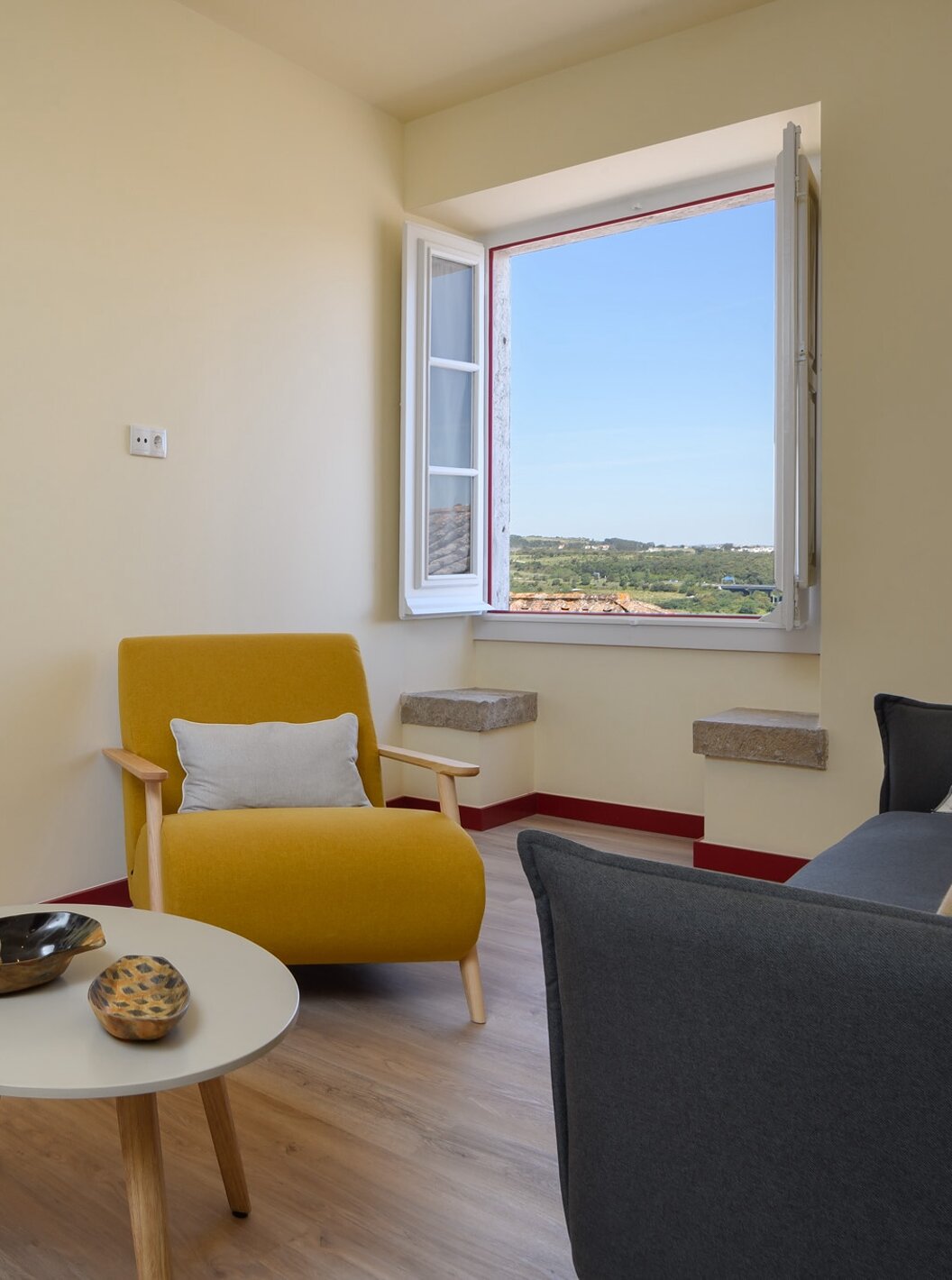 A Suite da Casa Lidador - Óbidos tem uma pequena sala com sofá , cadeira, mesa e apoio e uma janela com um banco em pedra