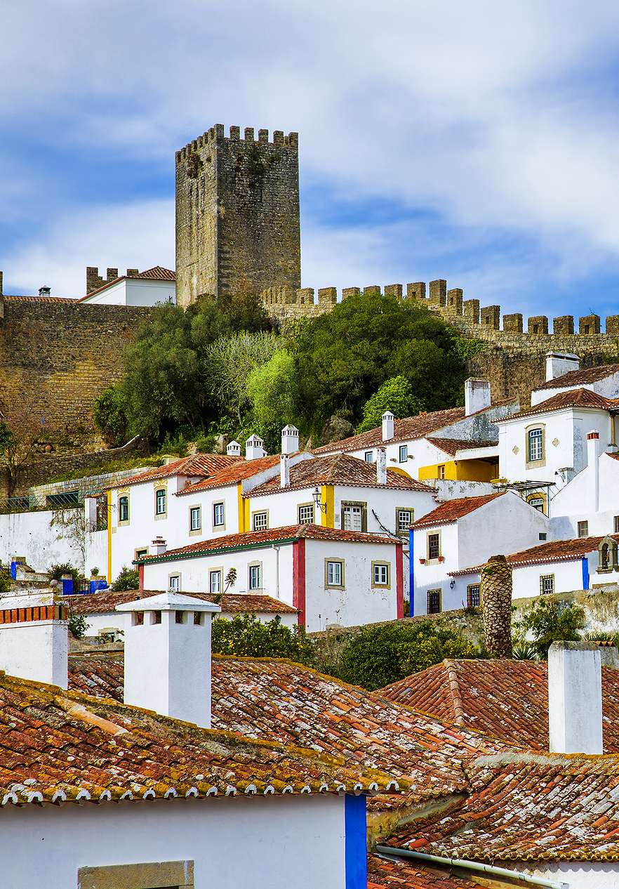 Vila de Óbidos, com várias casas brancas com riscas amarelas, azuis e vermelhas e o Castelo de Óbidos no fundo
