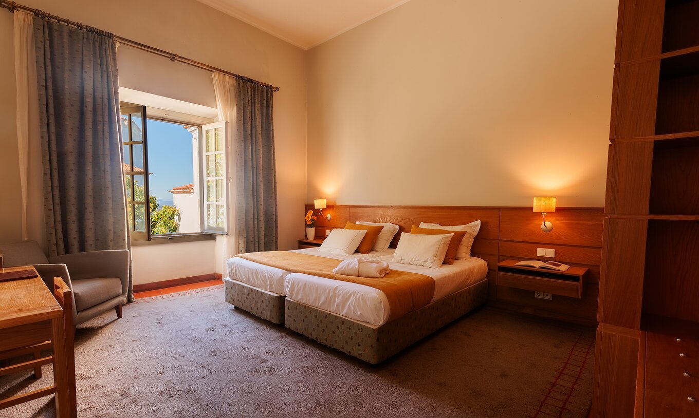 A Suite da Pousada Ourém tem uma cama de casa com colcha laranja e uma janela aberta ao lado