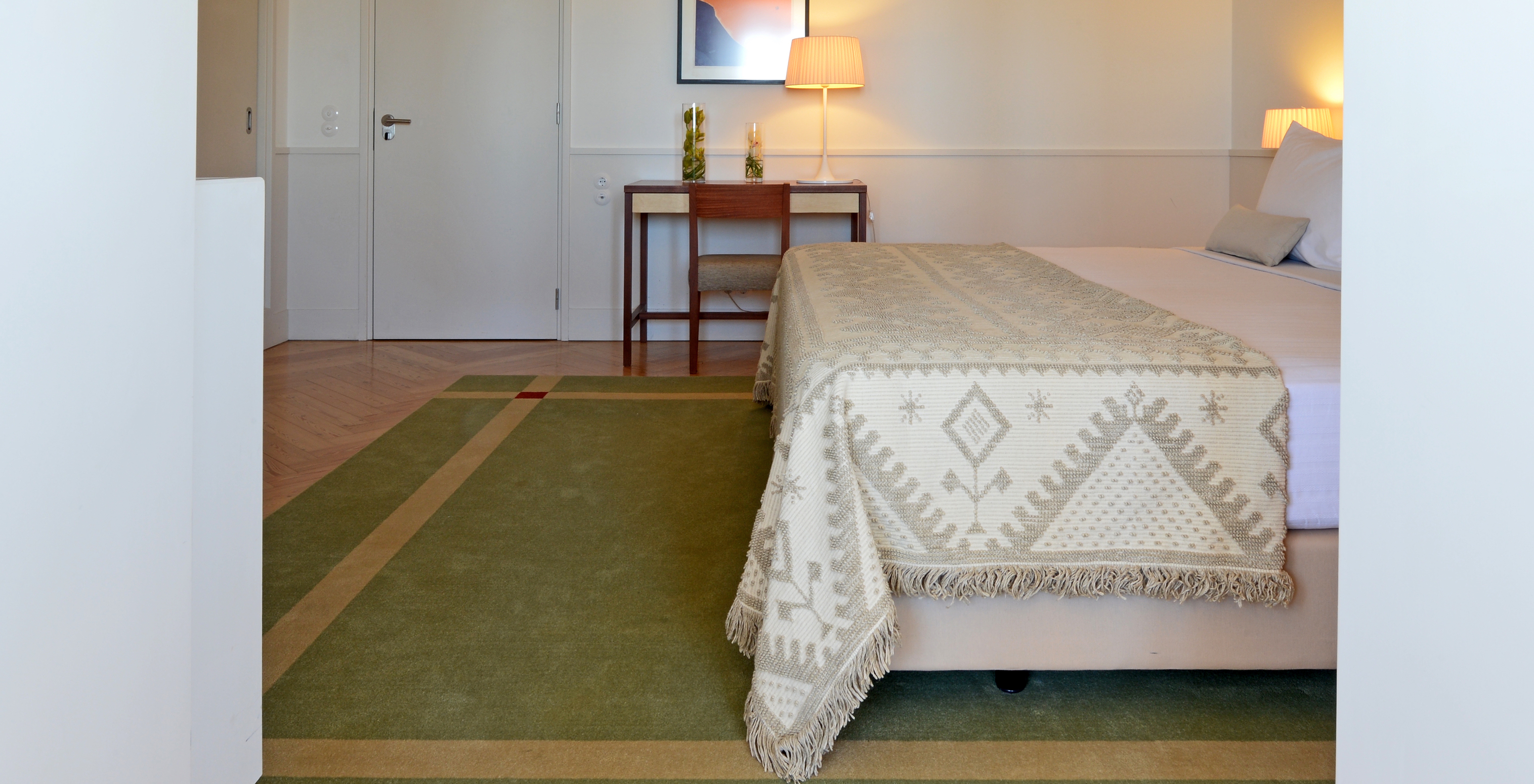 A Junior Suite da Pousada Serra da Estrela tem uma cama de casal com uma manta, uma secretária com uma cadeira e um quadro