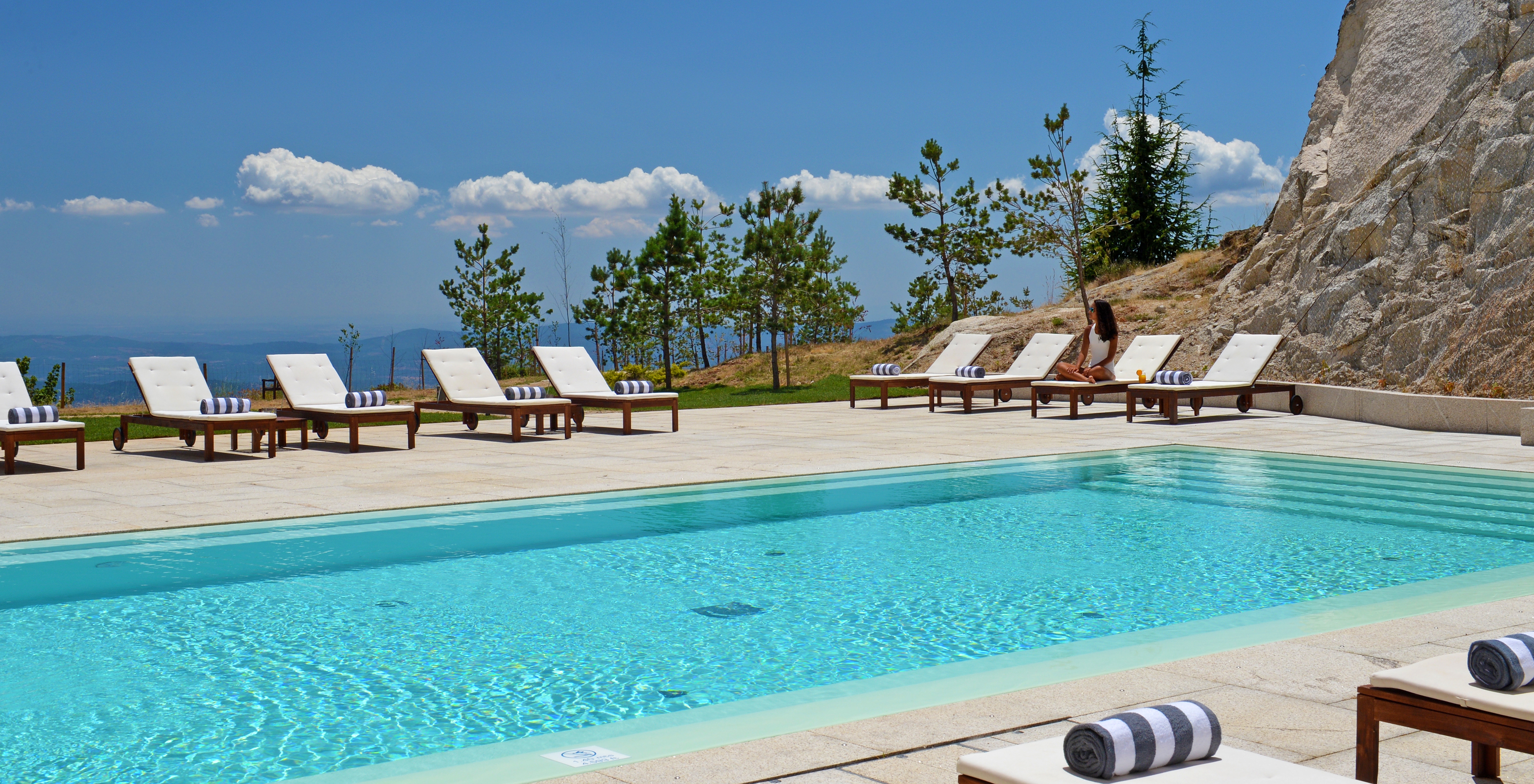 Piscina exterior de Hotel de Montanha no Centro de Portugal, com espreguiçadeiras com almofadas e vista para a Serra