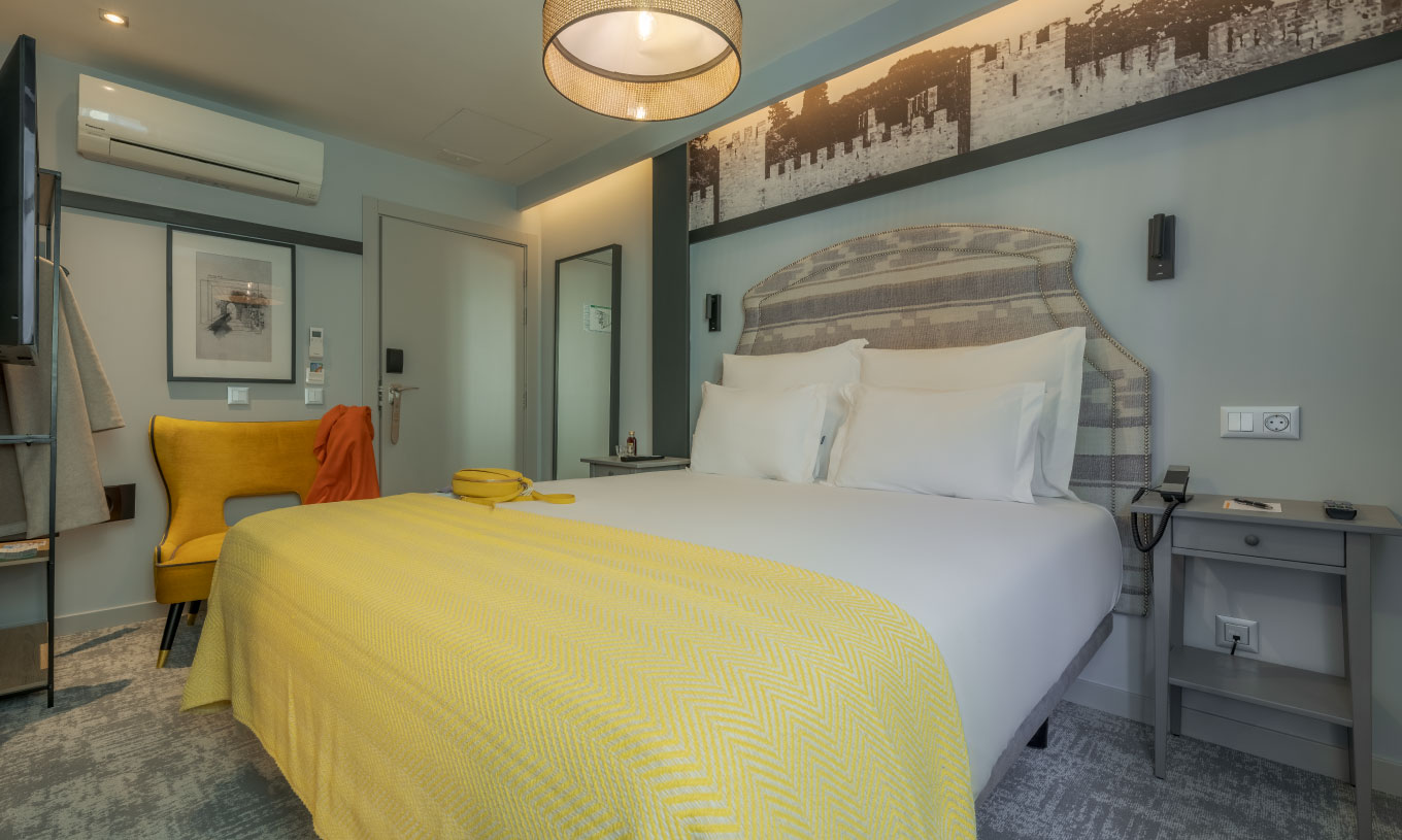 O Cozy da Pousada Alfama tem uma cama de casal com lençóis brancos e uma manta amarela e uma poltrona amarela