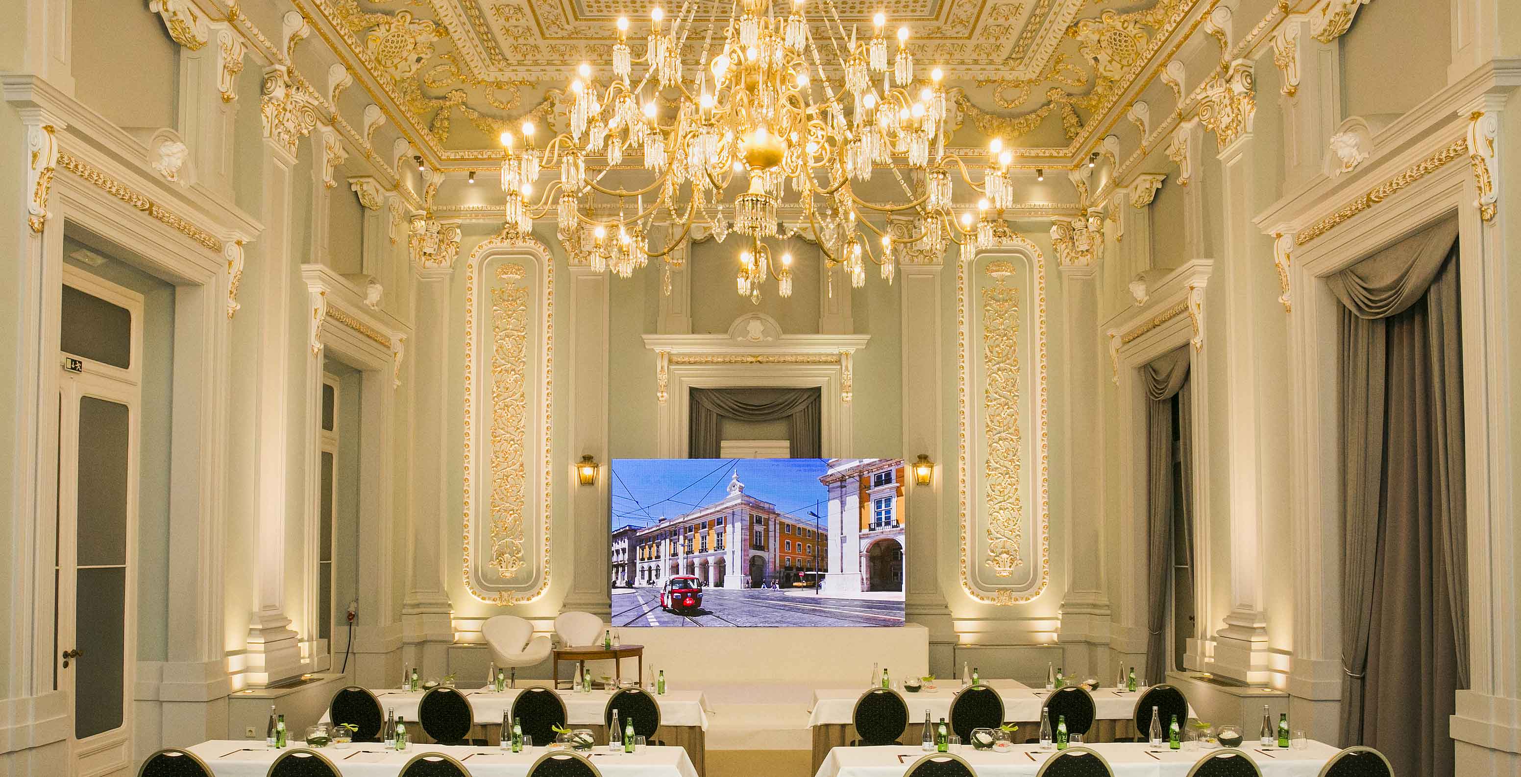 Salão de eventos elegante no hotel histórico na Baixa de Lisboa, com um lustre, detalhes dourados, mesas e cadeiras 