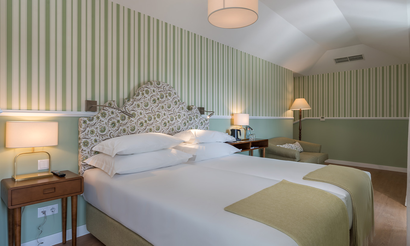 O Quarto Clássico do Pestana Churchill Bay tem uma cama de casal, papel de parede às riscas em tons verdes e um cadeirão