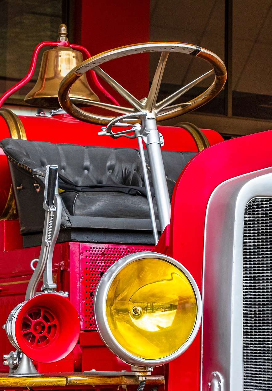 Detalhe de um antigo camião de bombeiros vermelho com volante, sino dourado e farol amarelo no Museu dos Bombeiros perto da Pousada Valença