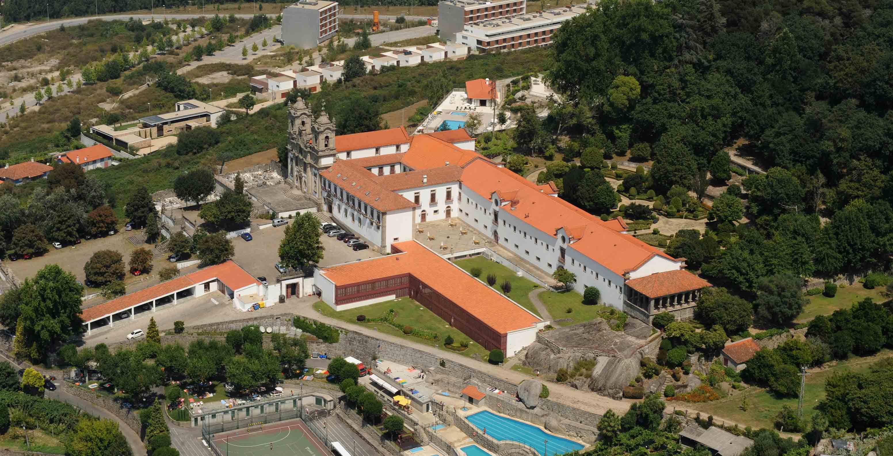 Vista aérea exterior da fachada da Pousada Mosteiro Guimarães, com estacionamento, piscina e jardins extensos. 