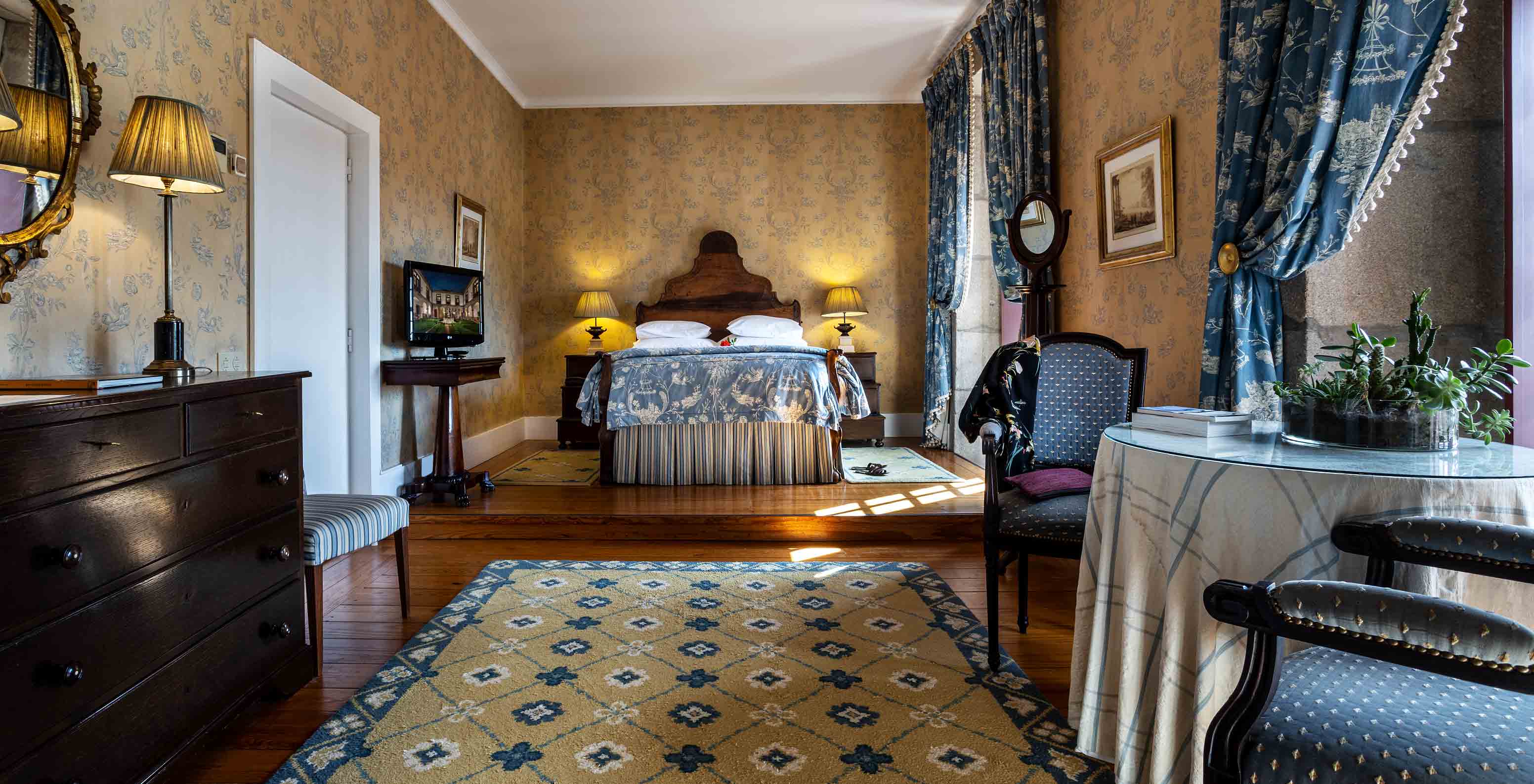 A Master Suite da Pousada Mosteiro Guimarães tem tons azuis, cama de casal, mesa e cadeiras e uma cómoda