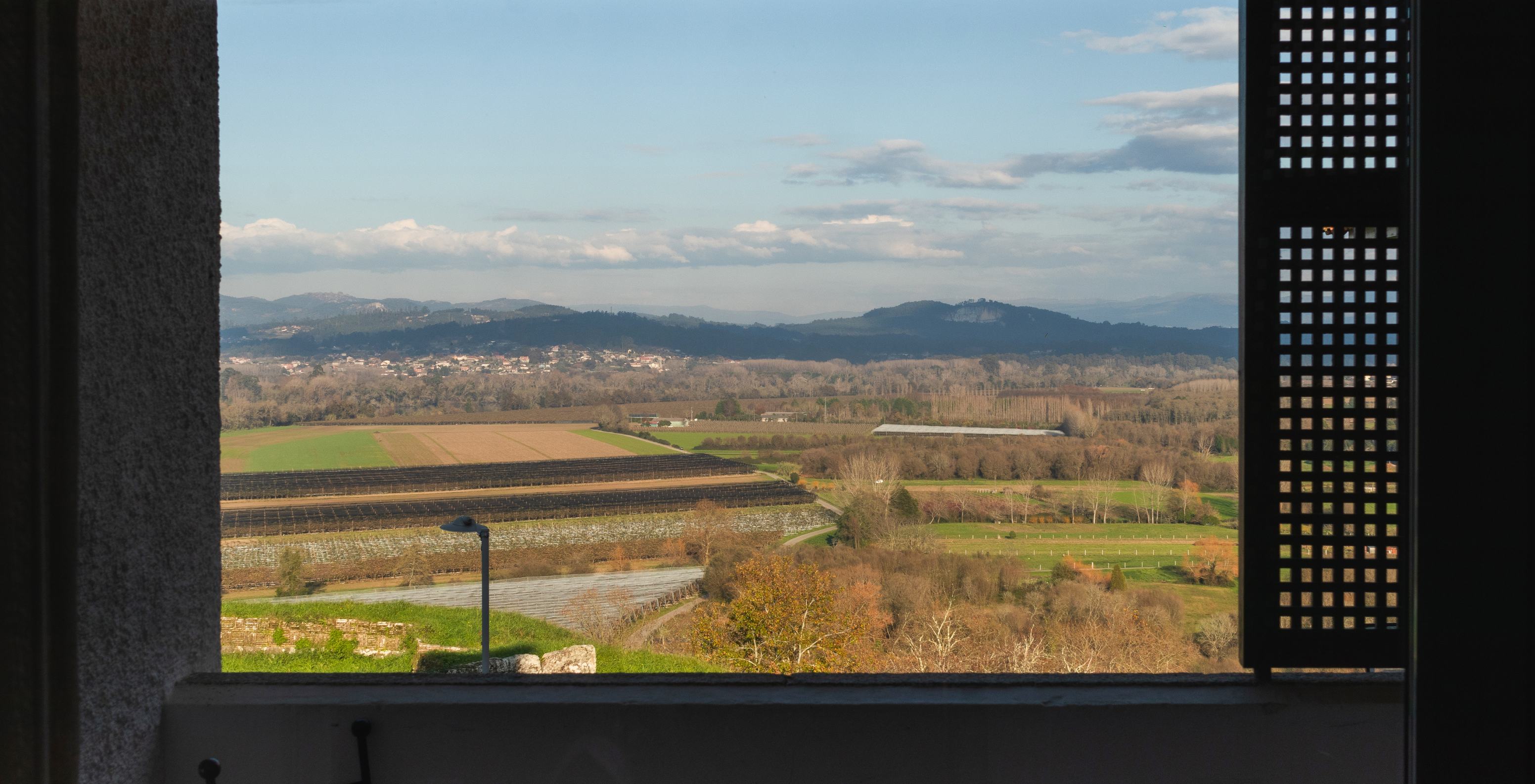 Vista panorâmica de campos verdes e montanhas ao longe a partir de uma varanda na Pousada de Valença