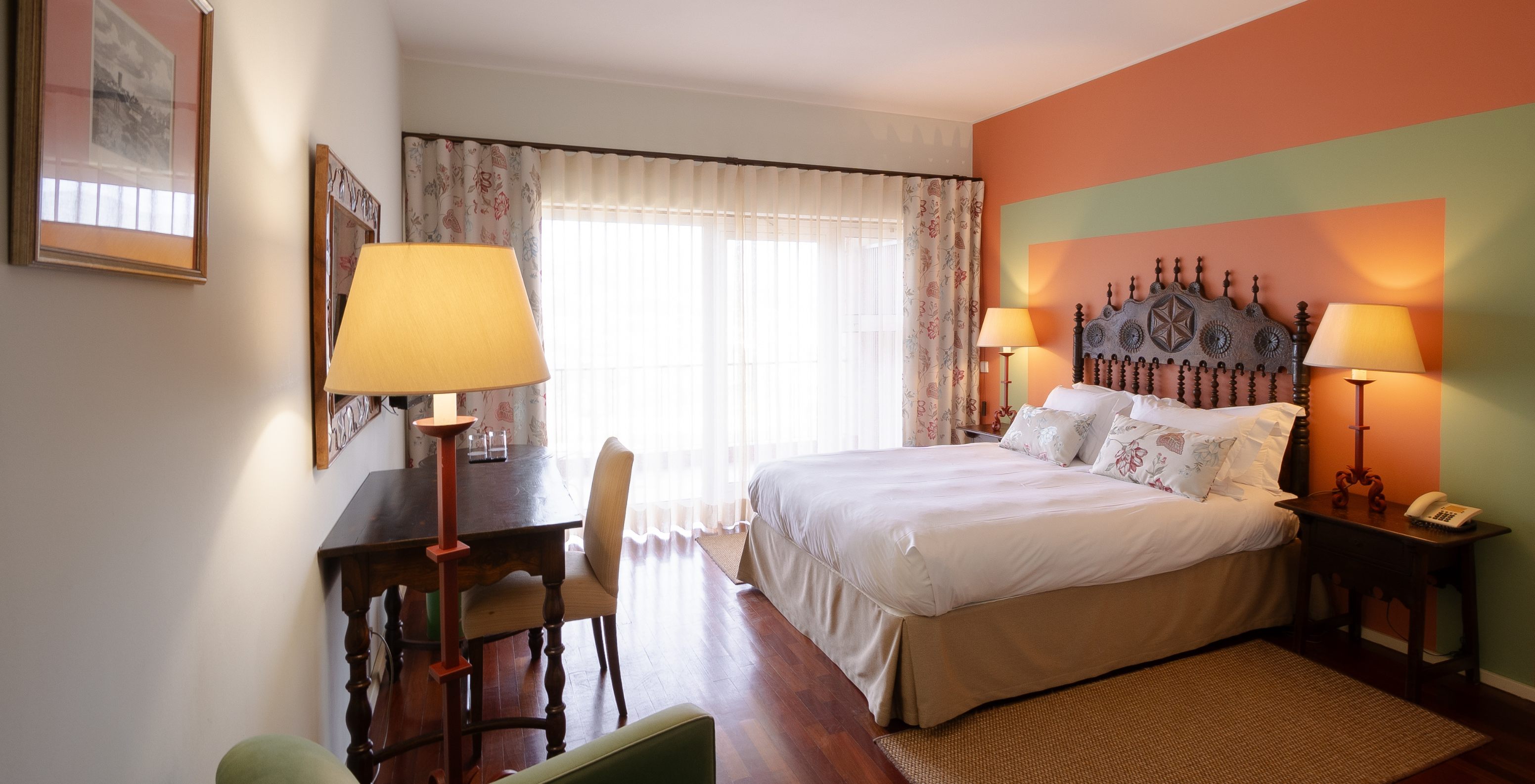 Quarto Superior com terraço na Pousada Valença, cama de casal, secretária e luz natural através das cortinas